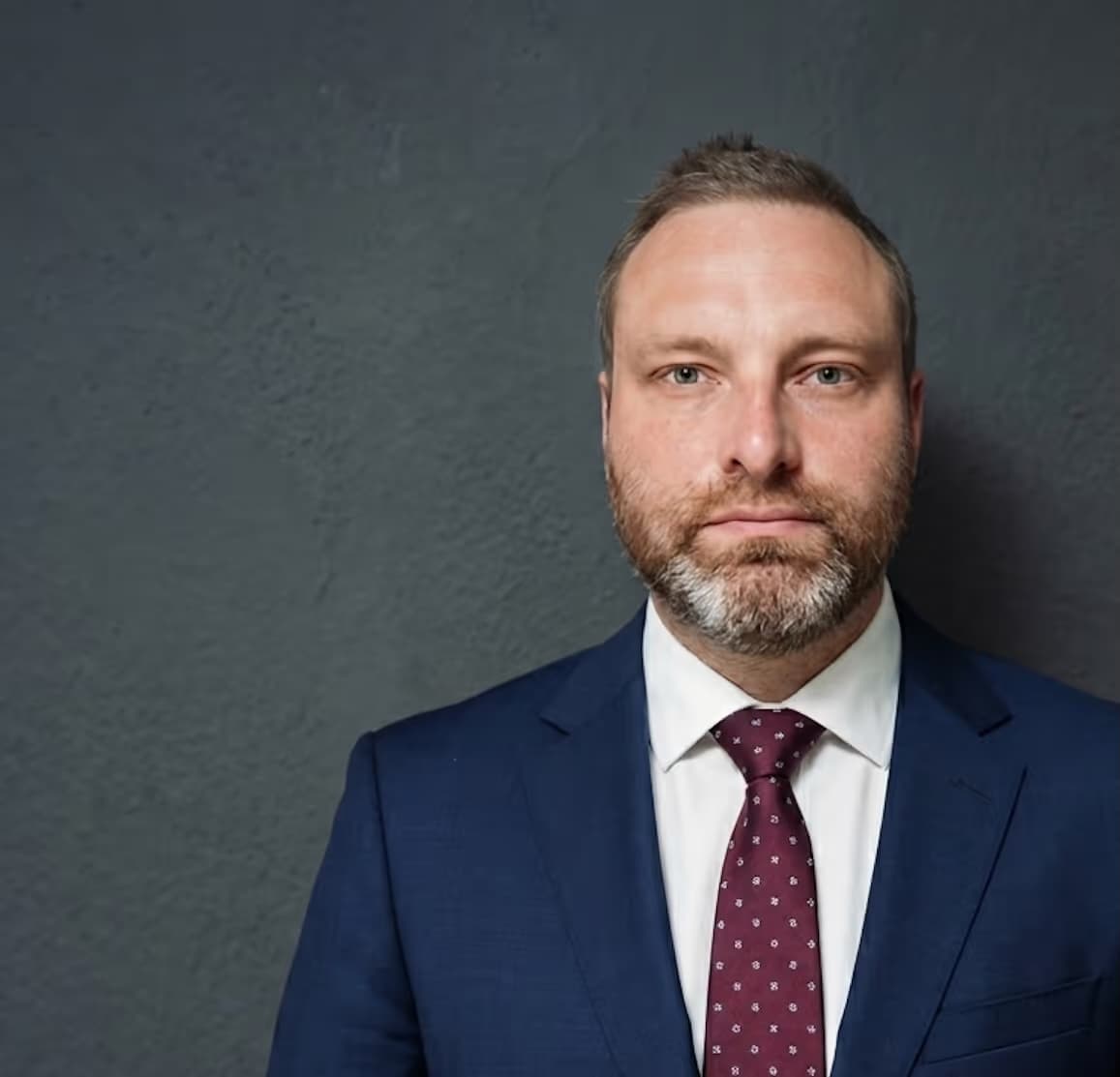 Carsten Schönberg im Anzug vor grauer Wand